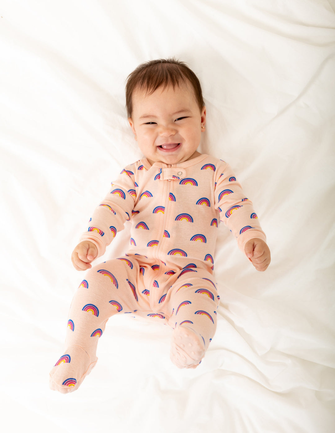 Baby wearing a pink rainbow onesie lying on a white blanket