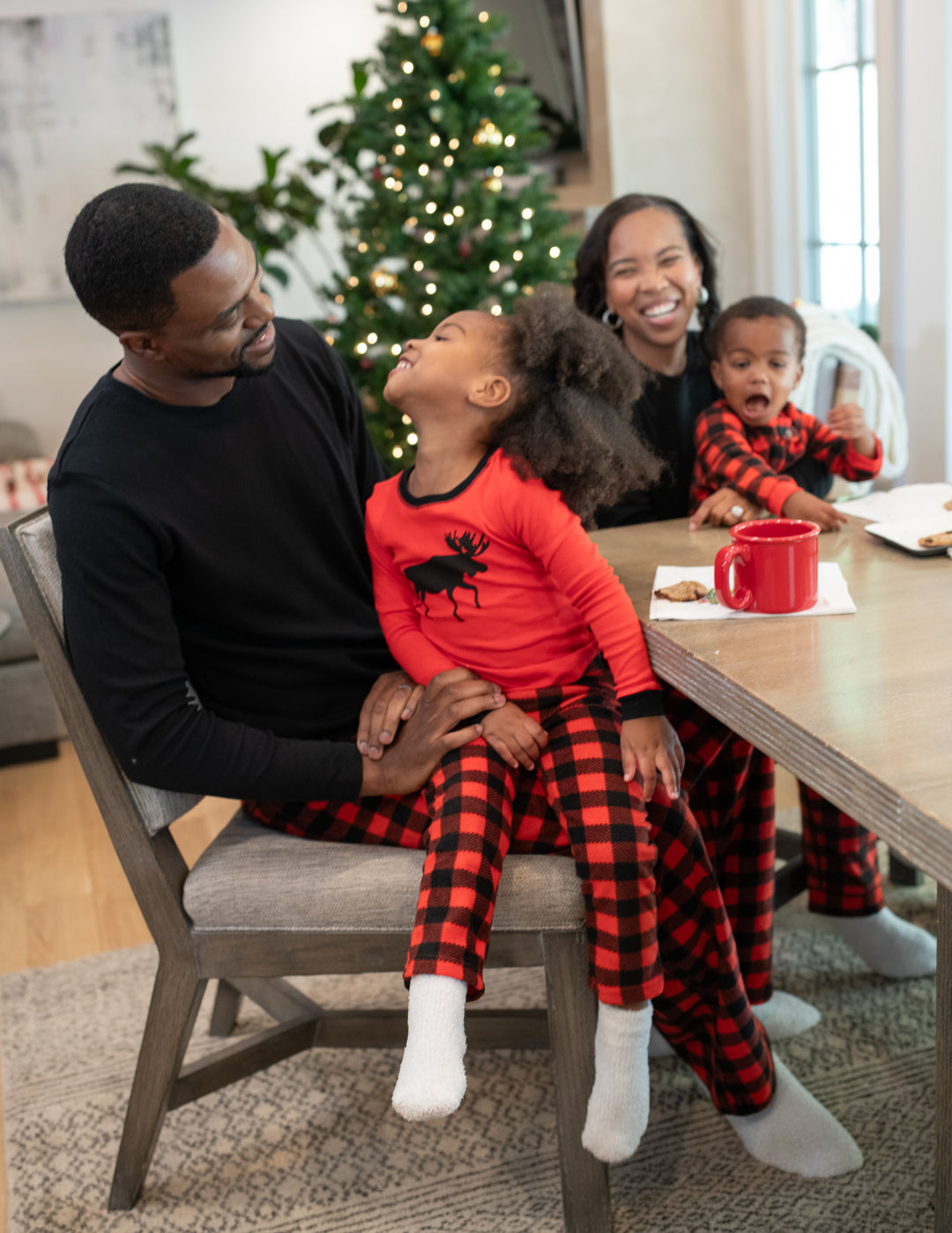 mom, dad, daughter, and baby wearing matching red & black plaid fleece moose pajamas