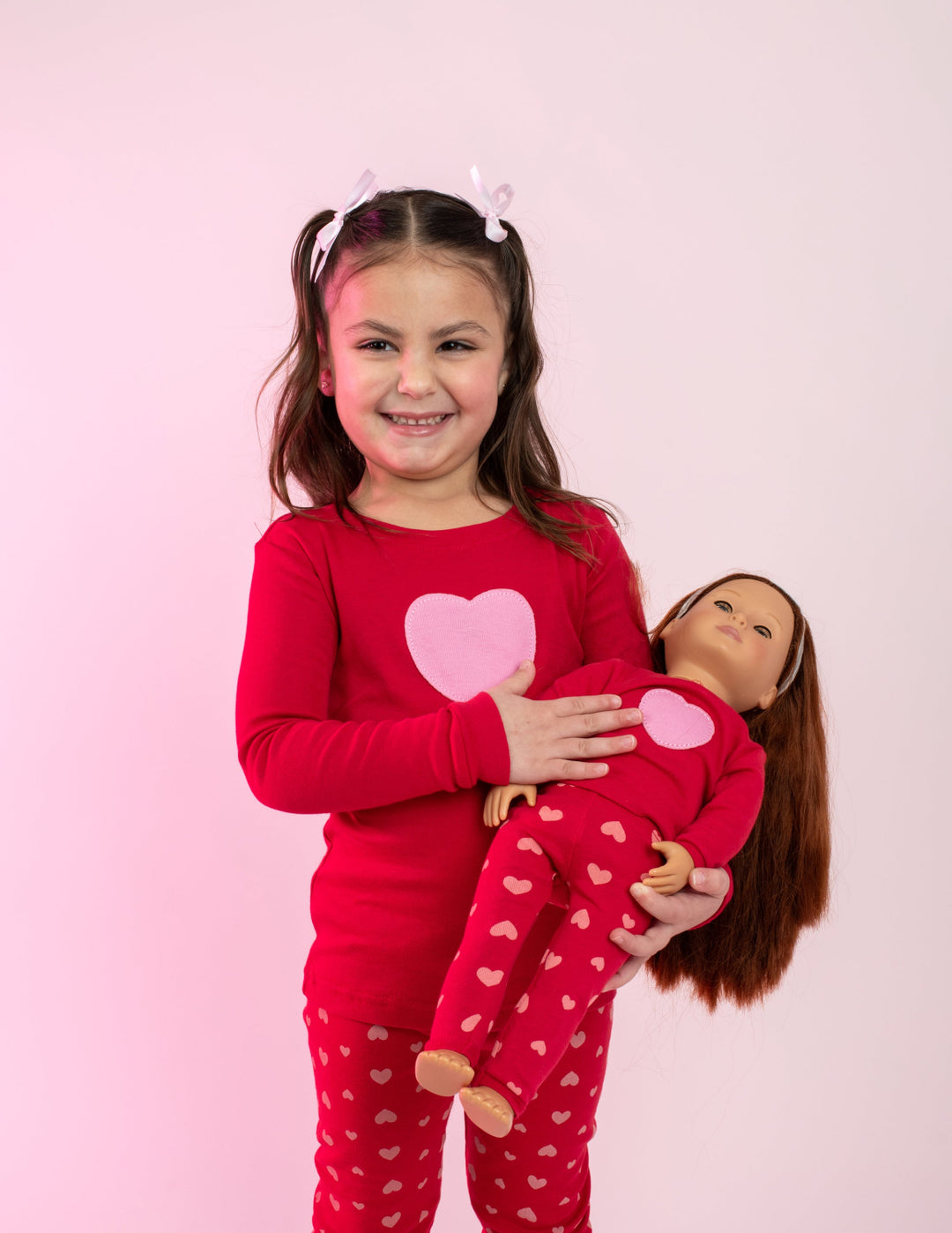 Girl in red heart pajamas holding a doll in matching pajamas
