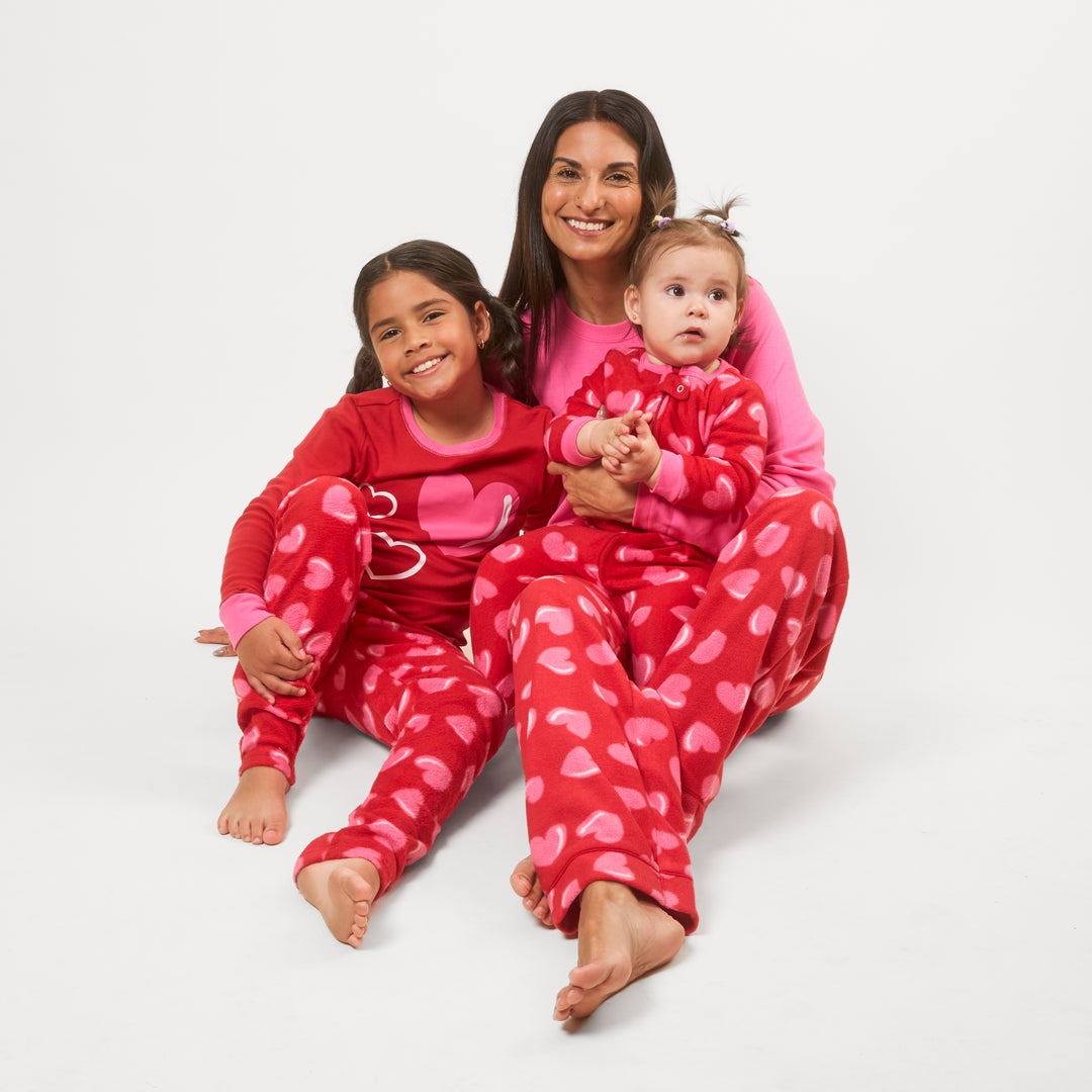 Woman and two children wearing red pajamas with pink hearts on a white background